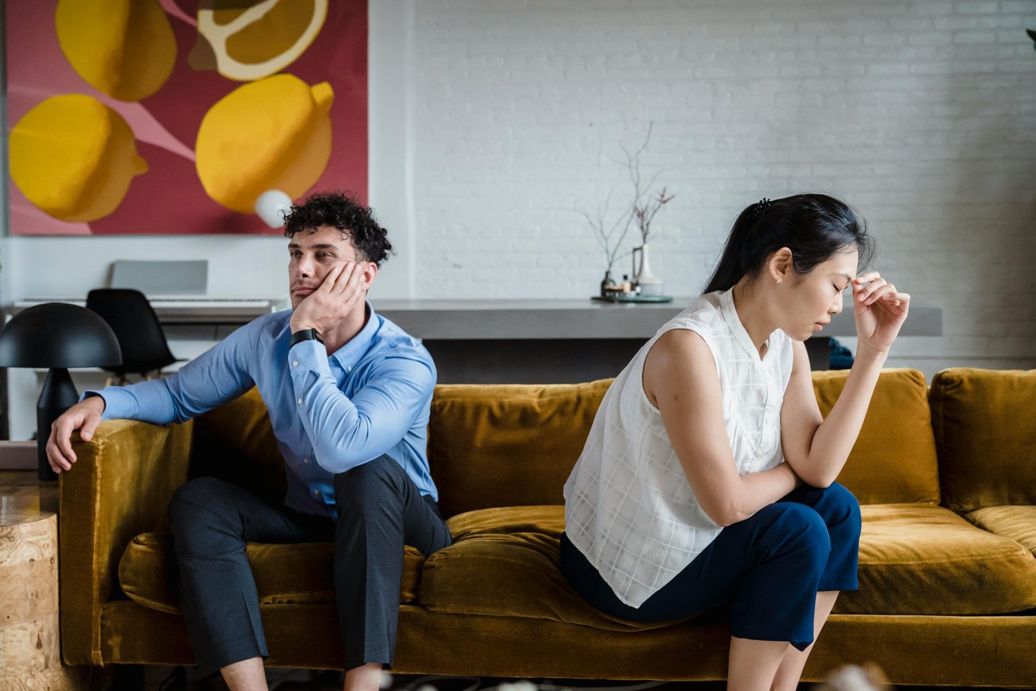 Couple sitting apart on a sofa, looking distressed