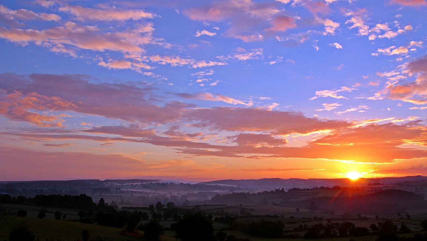 Sun setting over a distant landscape beneath a colorful sky