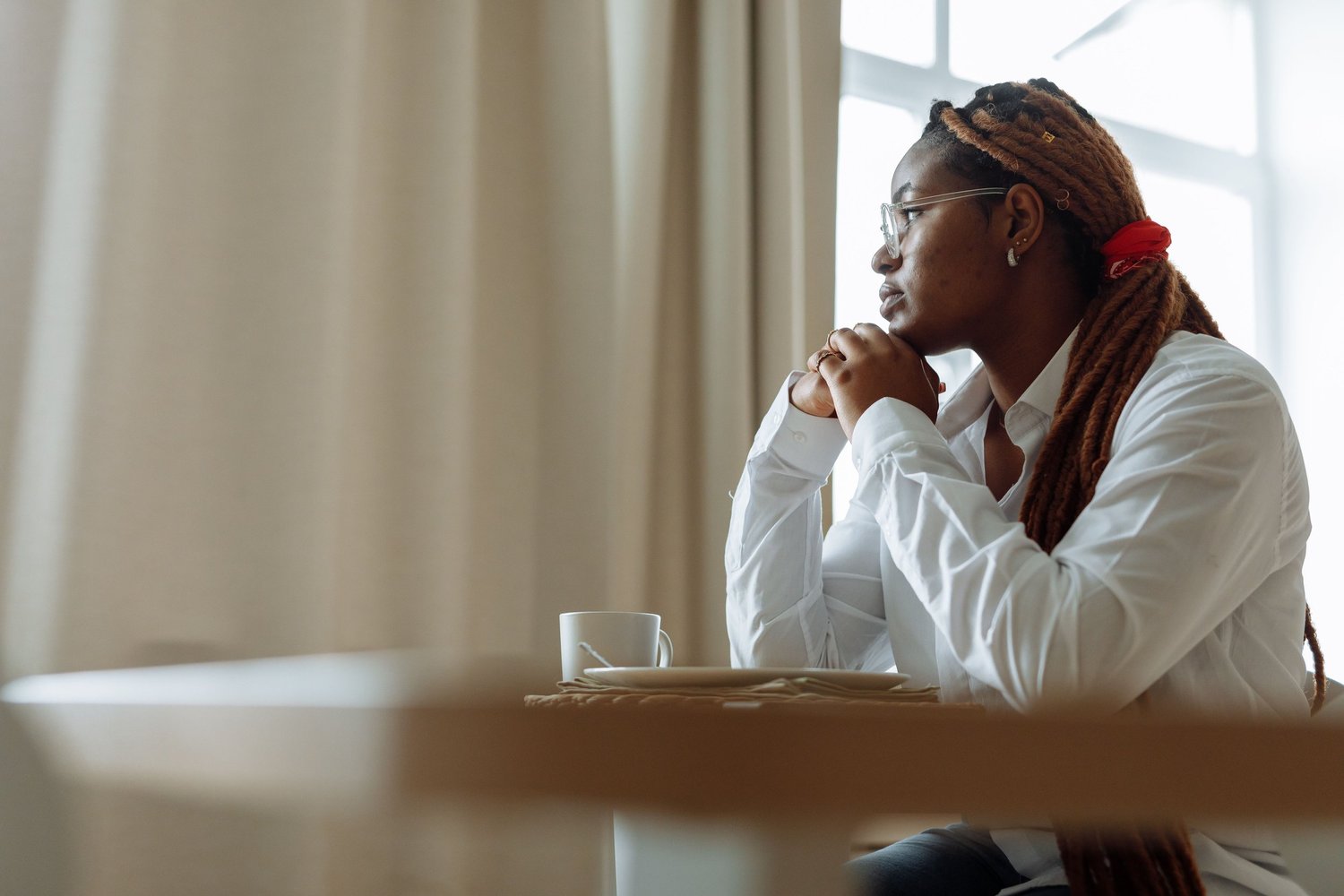 Person sitting alone by a window with a hand against their face