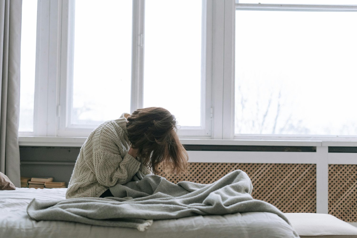 A woman sitting on her bed looking stressed and anxious, representing the emotional struggle of living with trichotillomania.