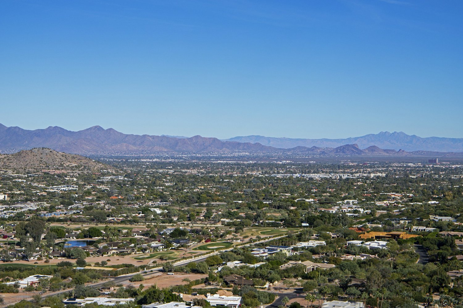 Aerial view of Arizona featuring residential homes nestled among desert landscapes, with mountain ranges and clear blue skies in the background.