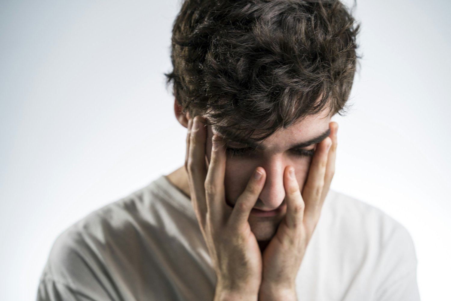 A man holding his face with both hands, eyes downcast, appearing deep in thought and emotionally overwhelmed, representing struggles related to OCD and PTSD.