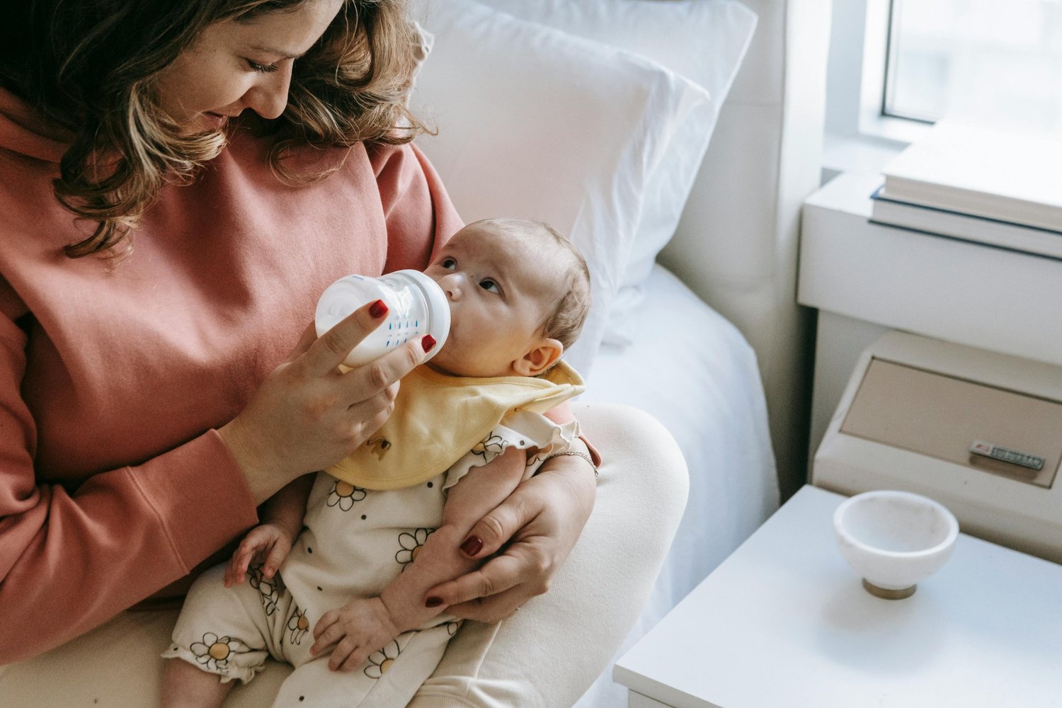 Parent bottle-feeding a baby while seated on a bed