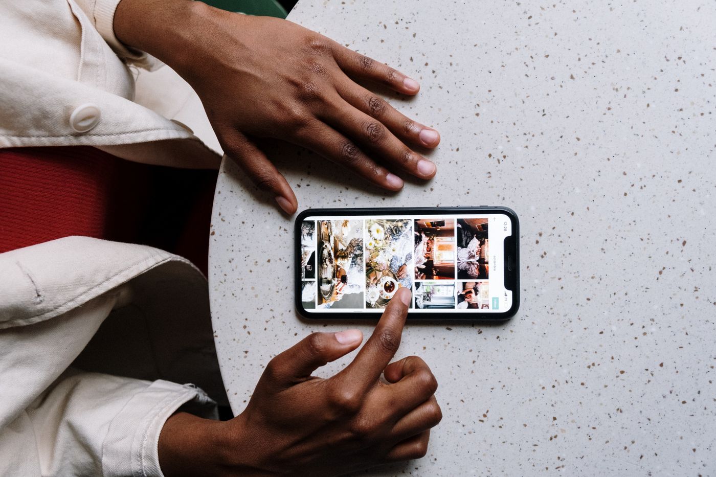 Hands using a smartphone to browse photos at a cafe table.