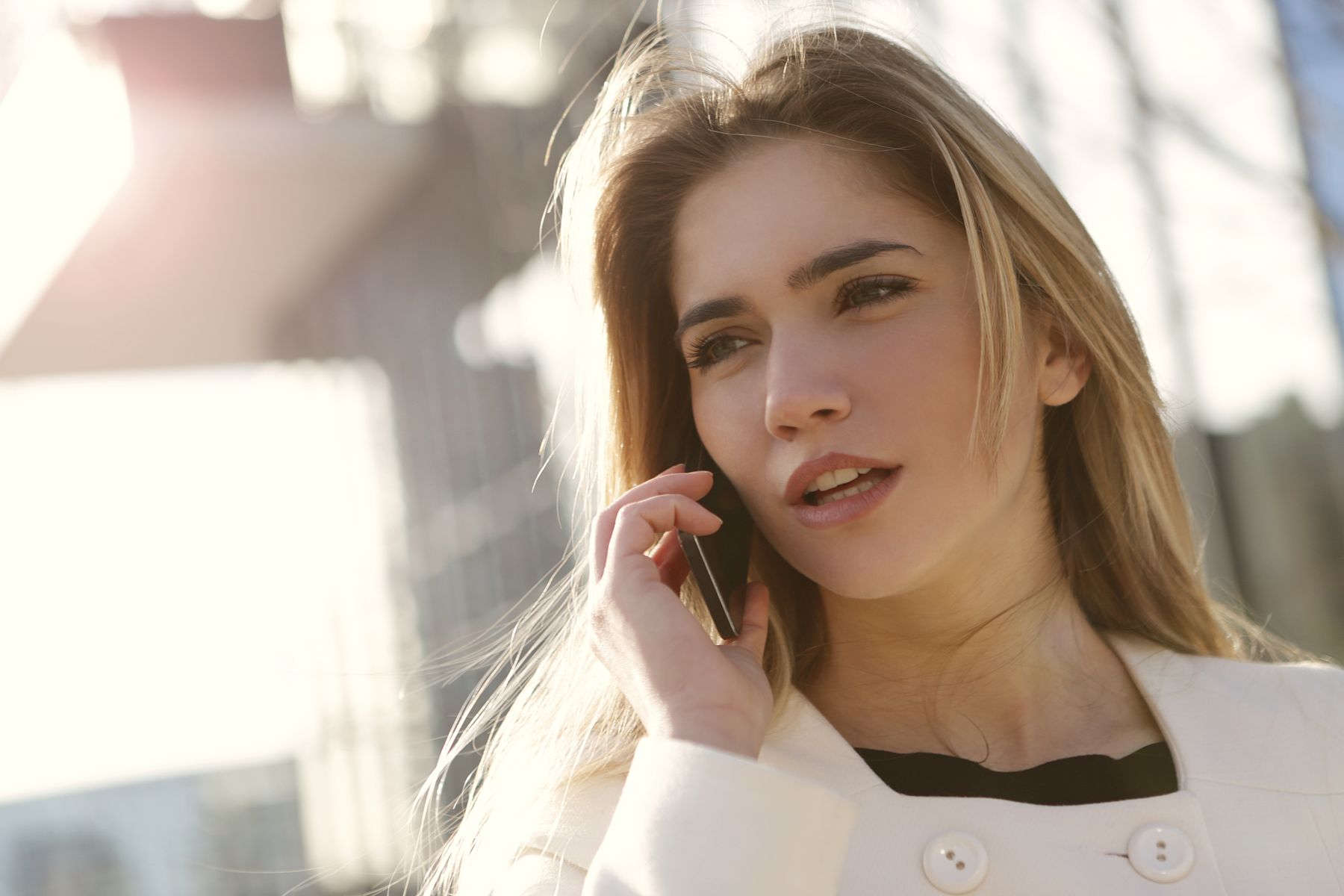 A woman holding a smartphone outdoors in daylight.