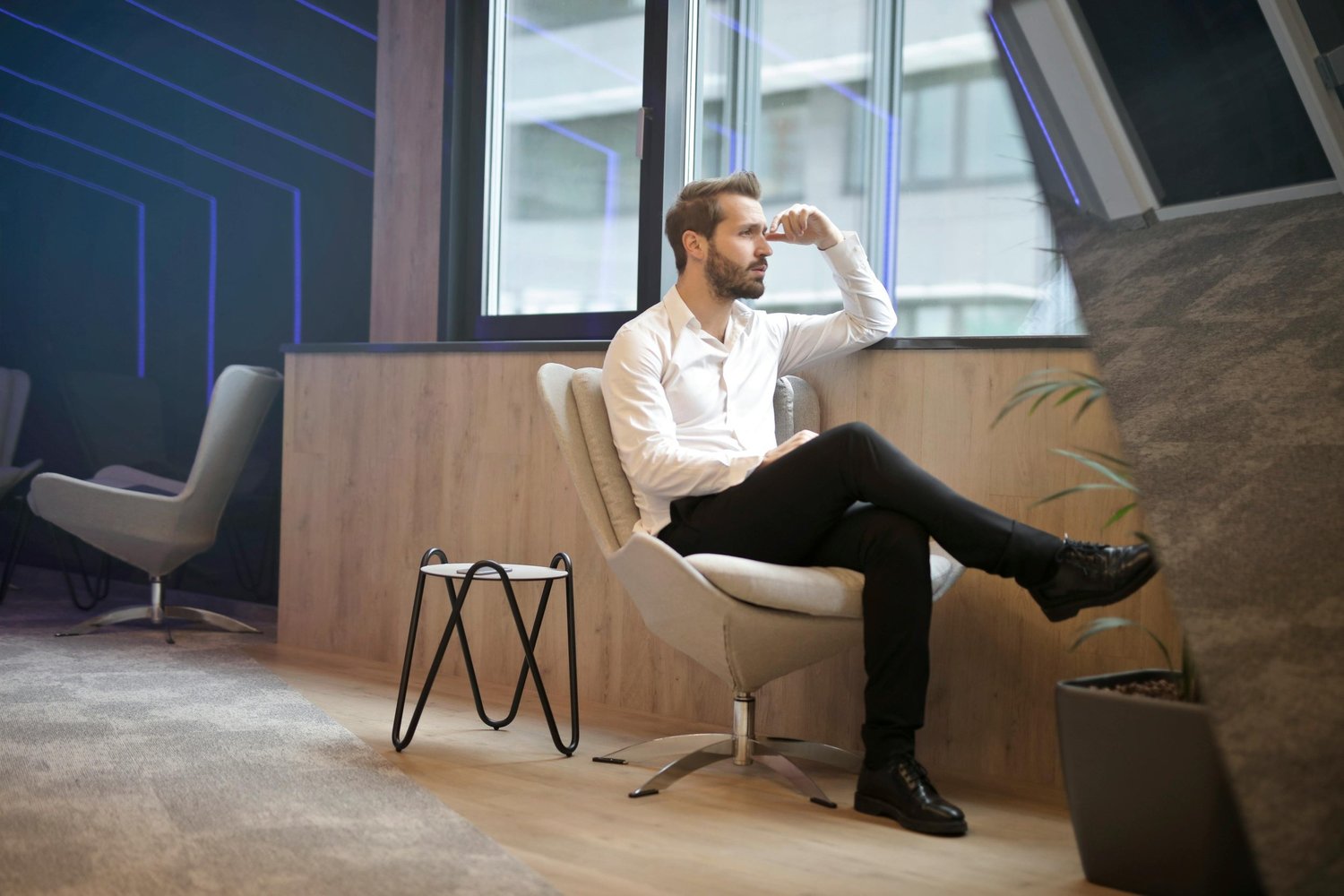 Man sitting beside a window, staring out with a tense, distant expression, appearing lost in intrusive thoughts and mental overwhelm.