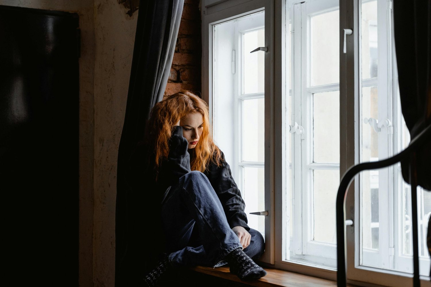 Person sitting alone on a windowsill looking outside