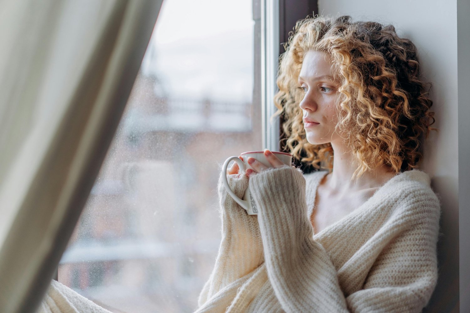 Woman calmly thinking by a window, reflecting on intrusive thoughts and mental health wellness