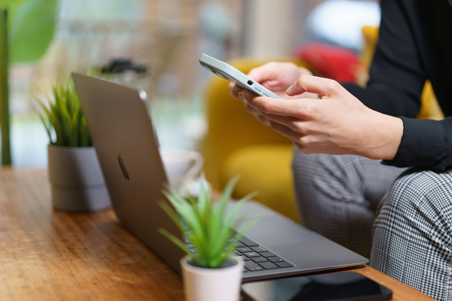Person holding a smartphone beside an open laptop