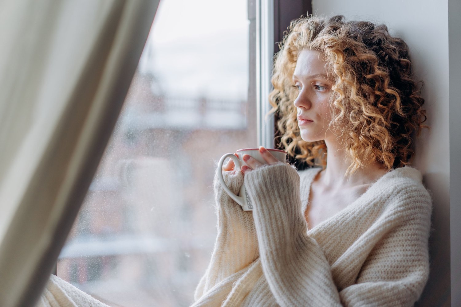 Woman looking thoughtfully out a window while reflecting on OCD recovery and mental health wellness.